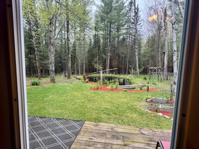 2733 Timberlane Trl, Grayling, MI 49738 - view of green lawn featuring a vegetable garden, a wooden deck, and a wooded view