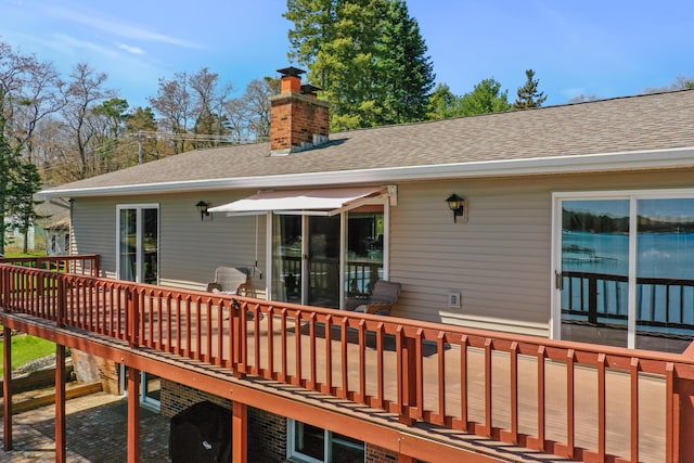 back of house with a deck, a chimney, and roof with shingles