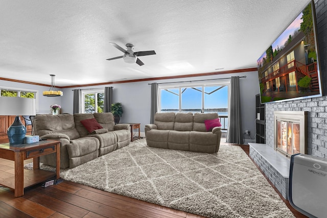 living area with crown molding, a ceiling fan, dark wood-type flooring, a brick fireplace, and a textured ceiling