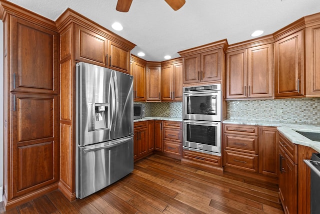 kitchen featuring appliances with stainless steel finishes, brown cabinets, dark wood-style floors, recessed lighting, and light stone countertops