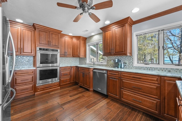 kitchen featuring appliances with stainless steel finishes, dark wood-type flooring, brown cabinetry, a sink, and backsplash