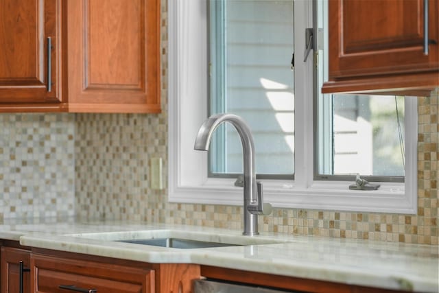 kitchen view of decorative backsplash, a sink, and light stone counters