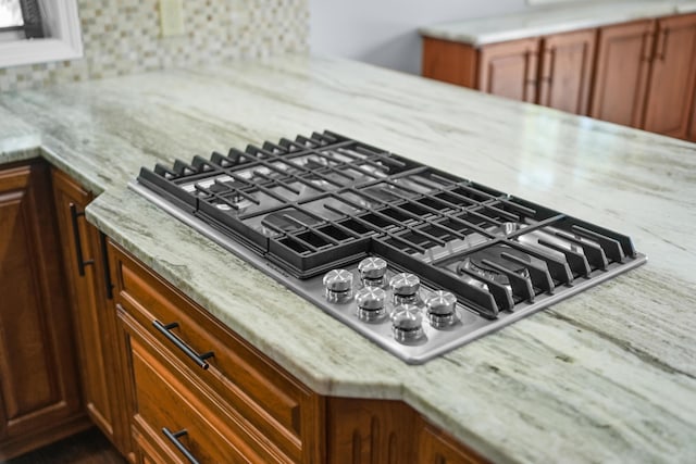 kitchen view of stainless steel gas stovetop, decorative backsplash, and light stone countertops