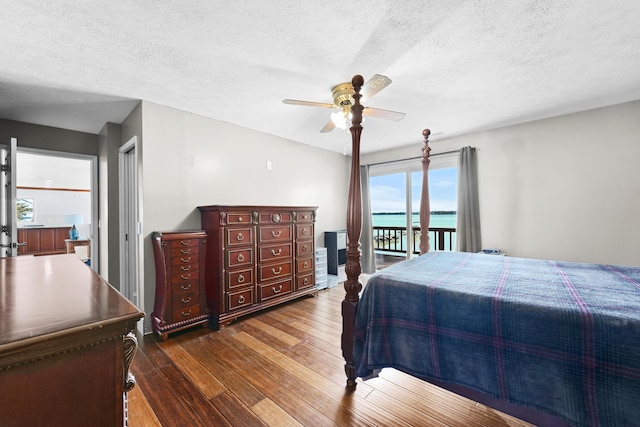 bedroom with access to outside, hardwood / wood-style flooring, a textured ceiling, ceiling fan, and a water view