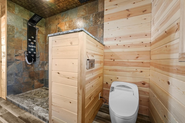 bathroom featuring tiled shower, wooden walls, and toilet