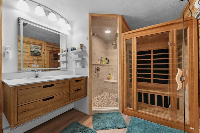 bathroom with a stall shower, wood finished floors, vanity, a relaxing sauna, and a textured ceiling
