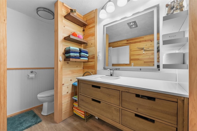 bathroom with toilet, wood finished floors, a wainscoted wall, and vanity