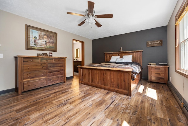 11758 Woodview Trl, Gaylord, MI 49735 - bedroom featuring wood finished floors, baseboards, baseboard heating, a ceiling fan, and ensuite bath
