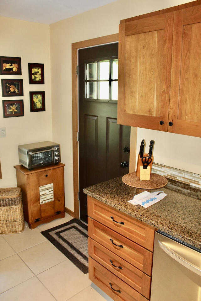 6475 W Legner Trl, Grayling, MI 49738 - kitchen with stainless steel dishwasher, light tile patterned floors, dark stone counters, and brown cabinetry