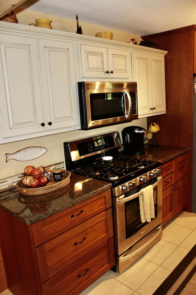 6475 W Legner Trl, Grayling, MI 49738 - kitchen with stainless steel appliances, light tile patterned floors, white cabinetry, dark stone countertops, and brown cabinets