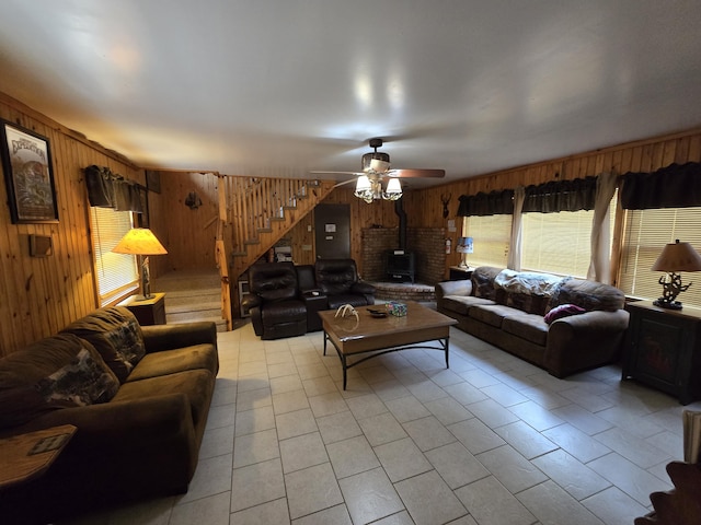 7912 Millecoquin Trl, Gaylord, MI 49735 - living area with wooden walls, a wood stove, stairway, a ceiling fan, and light tile patterned floors