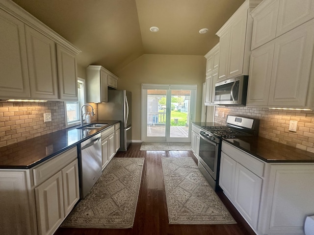 kitchen with stainless steel appliances, a sink, dark countertops, dark wood-style flooring, and white cabinetry