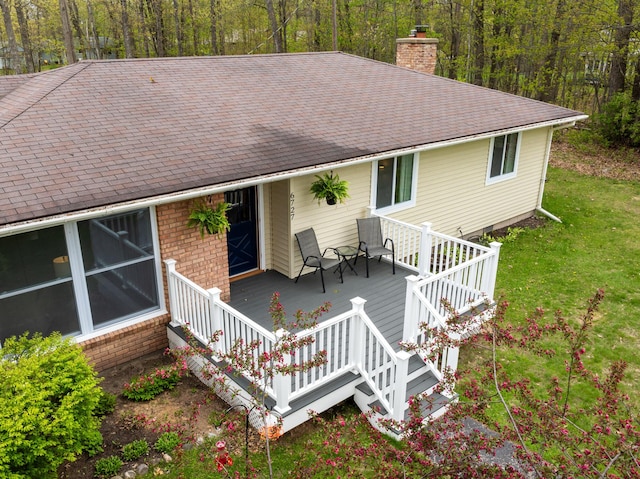 6727 Fisher Woods Rd, Indian River, MI 49749 - view of front of house featuring a chimney, a front lawn, a shingled roof, a wooden deck, and a view of trees