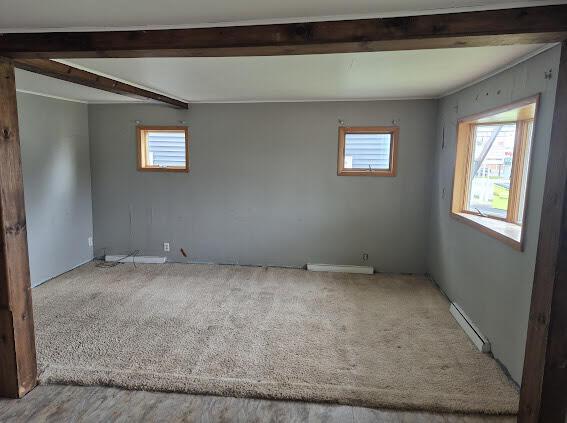 spare room featuring a baseboard heating unit, beamed ceiling, and carpet flooring