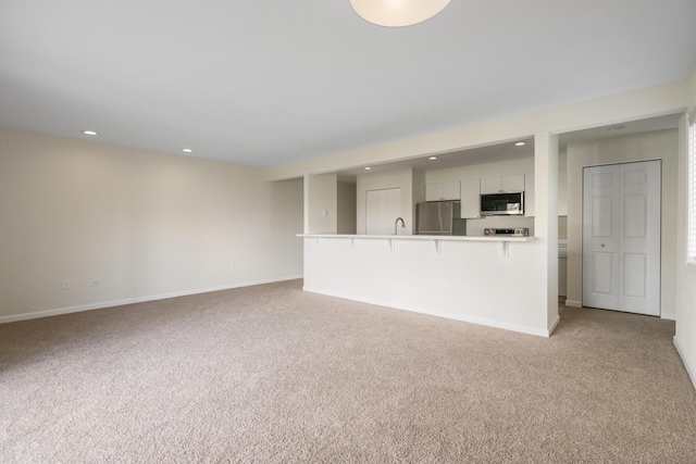 2067 Woods Ln, Petoskey, MI 49770 - unfurnished living room featuring light carpet, recessed lighting, baseboards, and a sink