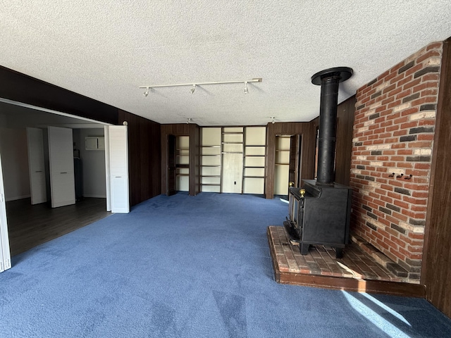 638 Snow Apple Ct, Cheboygan, MI 49721 - unfurnished living room with carpet floors, a wood stove, track lighting, a textured ceiling, and wood walls