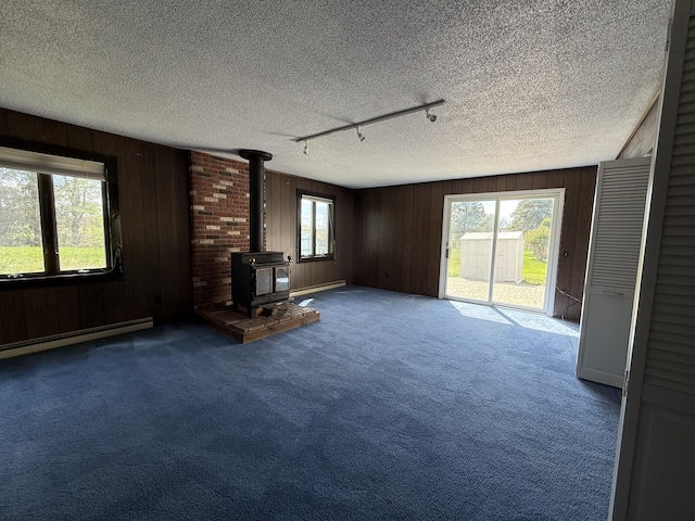 638 Snow Apple Ct, Cheboygan, MI 49721 - unfurnished living room featuring a wood stove, carpet flooring, wood walls, a baseboard radiator, and a textured ceiling