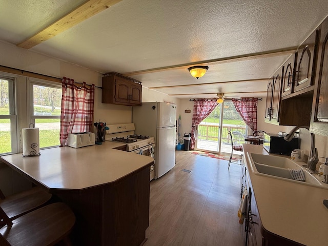 10117 M-18, Gladwin, MI 48624 - kitchen featuring white appliances, beamed ceiling, a textured ceiling, a sink, and a peninsula
