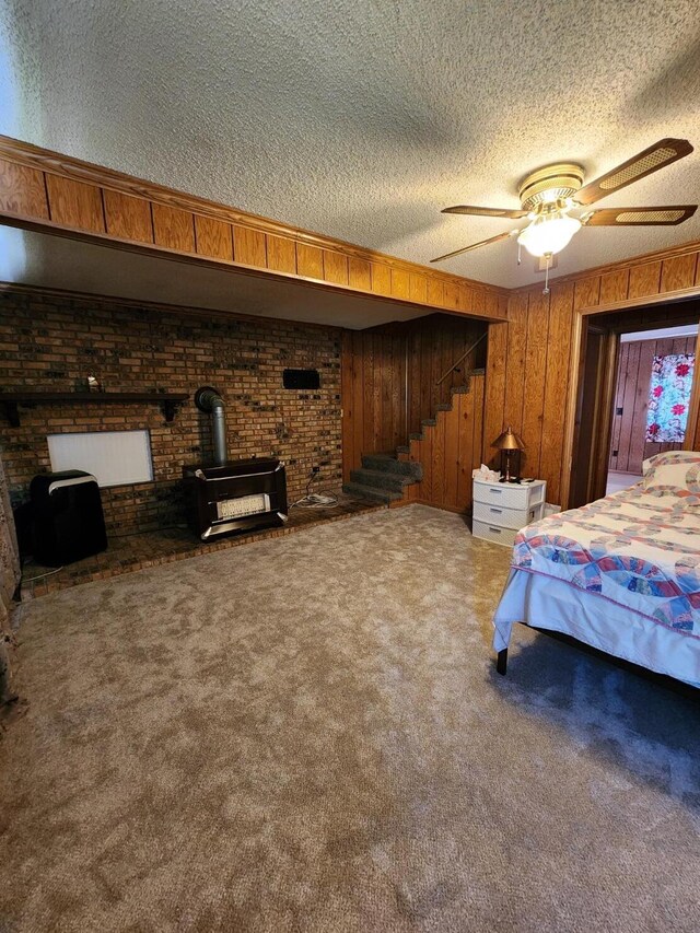 8881 Artesia Beach Rd, Saint Helen, MI 48656 - bedroom featuring a textured ceiling, a wood stove, wood walls, carpet flooring, and ceiling fan