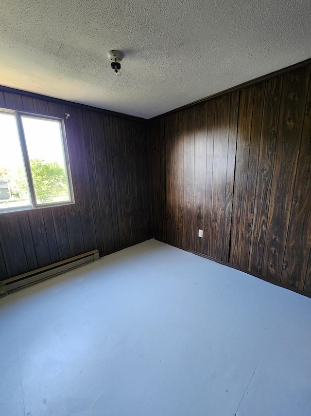 8881 Artesia Beach Rd, Saint Helen, MI 48656 - spare room with a baseboard heating unit, wood walls, concrete flooring, and a textured ceiling