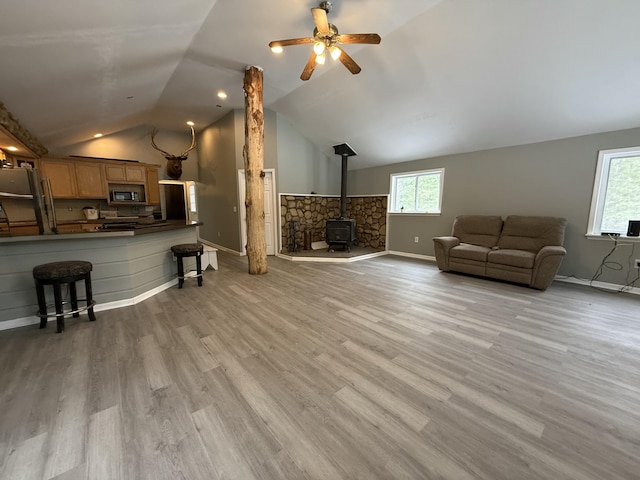4247 Racoon Trl, Lincoln, MI 48742 - living room featuring a wood stove, vaulted ceiling, a ceiling fan, light wood finished floors, and baseboards