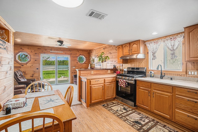 13042 Silver Lake Resort Rd, Wolverine, MI 49799 - kitchen featuring stainless steel gas range oven, under cabinet range hood, a sink, light wood-style flooring, and wood walls