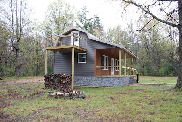 186 S Gerber Rd, Mio, MI 48647 - view of home's exterior with a balcony, stone siding, a lawn, and a view of trees