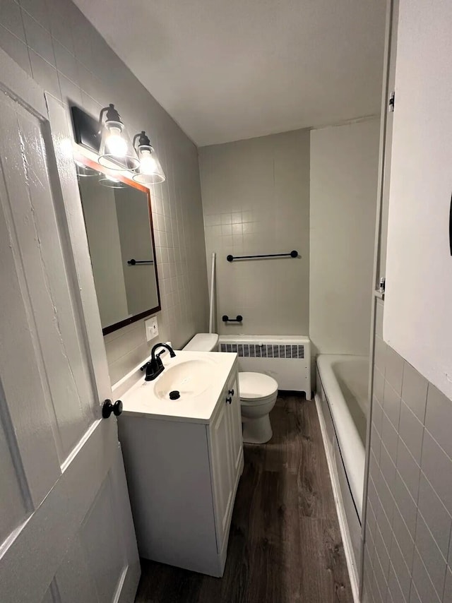 310 W Campbell St, Alpena, MI 49707 - full bathroom with radiator heating unit, tile walls, wood finished floors, toilet, and a tub to relax in
