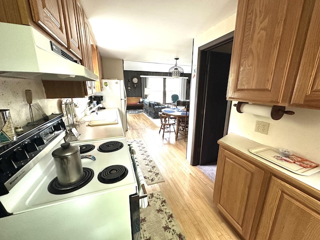 205 Beechwood Ave, Houghton Lake, MI 48629 - kitchen featuring white appliances, under cabinet range hood, light wood-style flooring, and brown cabinetry