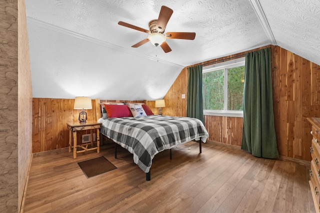 7028 Merrio Rd, Grayling, MI 49738 - bedroom with wooden walls, vaulted ceiling, hardwood / wood-style flooring, a textured ceiling, and a ceiling fan