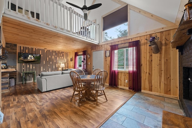 7028 Merrio Rd, Grayling, MI 49738 - dining space featuring wood walls, ceiling fan, a fireplace, high vaulted ceiling, and baseboards