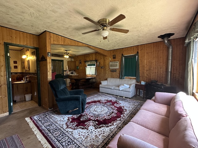 269 Dixson Dr, Grayling, MI 49738 - living room with a ceiling fan, wood walls, a wood stove, a wall mounted AC, and a textured ceiling