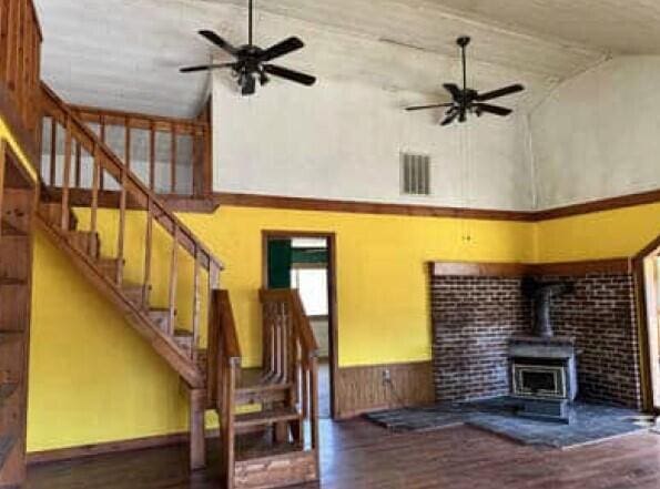 29098 W H 40, Moran, MI 49760 - unfurnished living room with high vaulted ceiling, a wood stove, ceiling fan, stairway, and a wainscoted wall