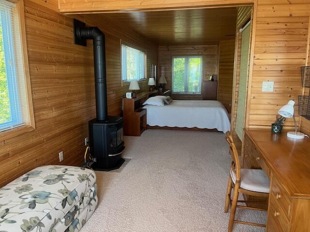 3199 S Lake Shore Dr, Bois Blanc, MI 49775 - carpeted bedroom with wood walls, a wood stove, and wooden ceiling