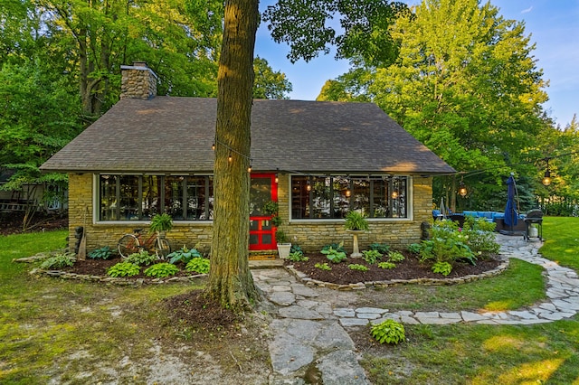 4423 Island View Dr, Gaylord, MI 49735 - view of front of house with stone siding, a shingled roof, a chimney, and a patio area