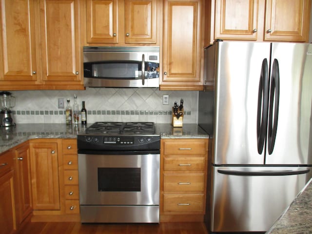 5622 Vacationland Dr, Lewiston, MI 49756 - kitchen featuring appliances with stainless steel finishes, decorative backsplash, stone countertops, and brown cabinetry