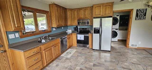 2460 Hamilton Rd, Alpena, MI 49707 - kitchen with stainless steel appliances, a sink, stacked washing machine and dryer, dark countertops, and brown cabinets