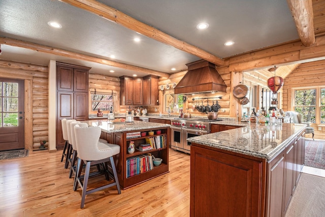 10924 E Grand Lake Rd, Presque Isle, MI 49777 - kitchen with range with two ovens, rustic walls, premium range hood, beam ceiling, and light wood-style floors