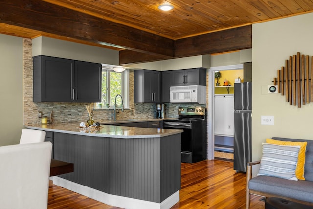 6192 Wilderness Dr, Mancelona, MI 49659 - kitchen with black range with electric stovetop, white microwave, freestanding refrigerator, a sink, and a peninsula