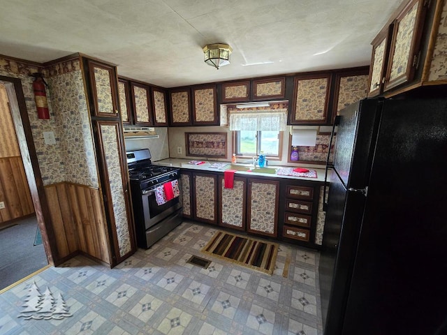 3557 Penn Rd, Lewiston, MI 49756 - kitchen with gas stove, freestanding refrigerator, wallpapered walls, and light countertops