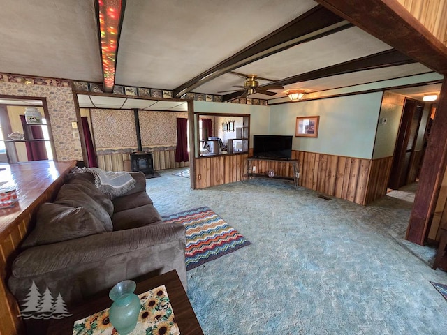 3557 Penn Rd, Lewiston, MI 49756 - living room with a wood stove, a wainscoted wall, carpet flooring, ceiling fan, and beamed ceiling