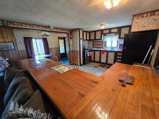 3557 Penn Rd, Lewiston, MI 49756 - kitchen featuring stainless steel gas stove, freestanding refrigerator, wallpapered walls, wood counters, and a wainscoted wall