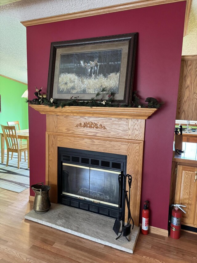 1154 M-72 W, Barton City, MI 48705 - detailed view of a glass covered fireplace, a fire extinguisher, wood finished floors, a textured ceiling, and ornamental molding
