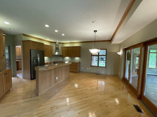 164 Invitational Dr, Gaylord, MI 49735 - kitchen featuring black fridge, wall chimney exhaust hood, crown molding, light wood-style flooring, and an island with sink