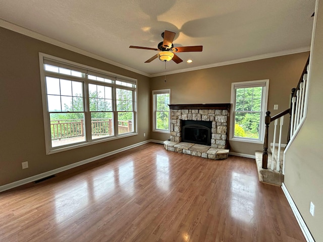 N1746 Smith Rd, Saint Ignace, MI 49781 - unfurnished living room with wood finished floors, ceiling fan, crown molding, stairway, and a stone fireplace