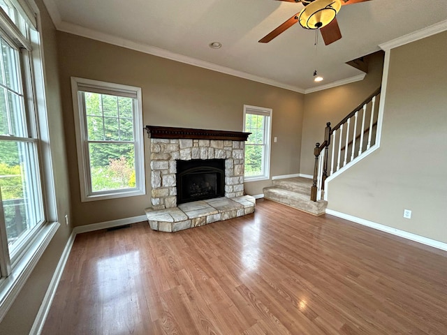 N1746 Smith Rd, Saint Ignace, MI 49781 - unfurnished living room featuring wood finished floors, crown molding, ceiling fan, a stone fireplace, and stairs