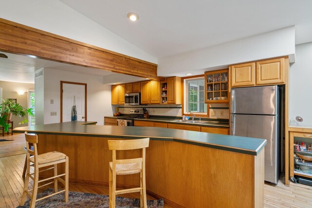 9707 Rogers Rd, Alanson, MI 49706 - kitchen with appliances with stainless steel finishes, light wood-style flooring, dark countertops, lofted ceiling, and a kitchen bar