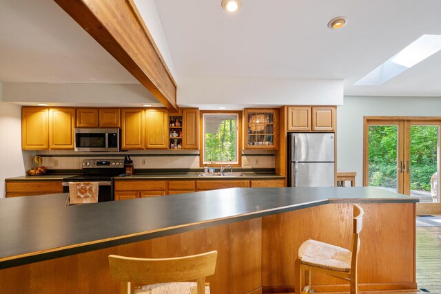 9707 Rogers Rd, Alanson, MI 49706 - kitchen featuring appliances with stainless steel finishes, a skylight, dark countertops, brown cabinets, and backsplash