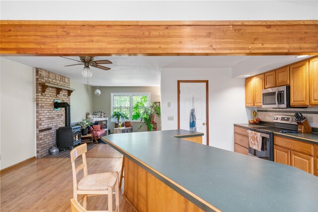 9707 Rogers Rd, Alanson, MI 49706 - kitchen with appliances with stainless steel finishes, a ceiling fan, a wood stove, light wood-style flooring, and tasteful backsplash