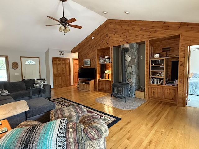 1058 Marlas Way, Cheboygan, MI 49721 - living area featuring wooden walls, a wood stove, a ceiling fan, wood finished floors, and high vaulted ceiling